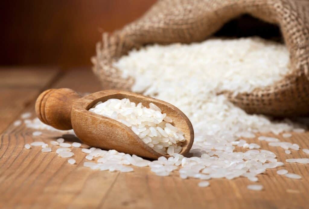 White rice in a sack and wooden scoops on wooden background.