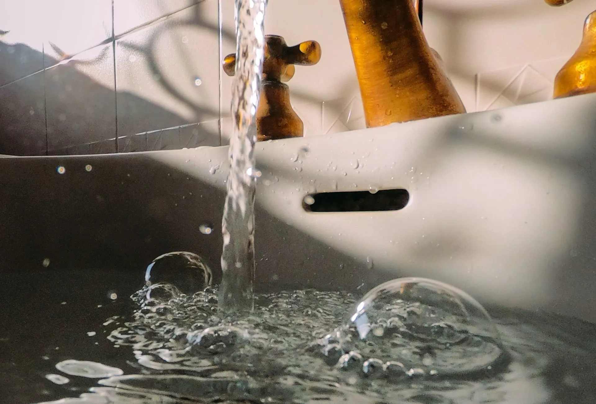 Water running from a bronze tap into a ceramic sink.