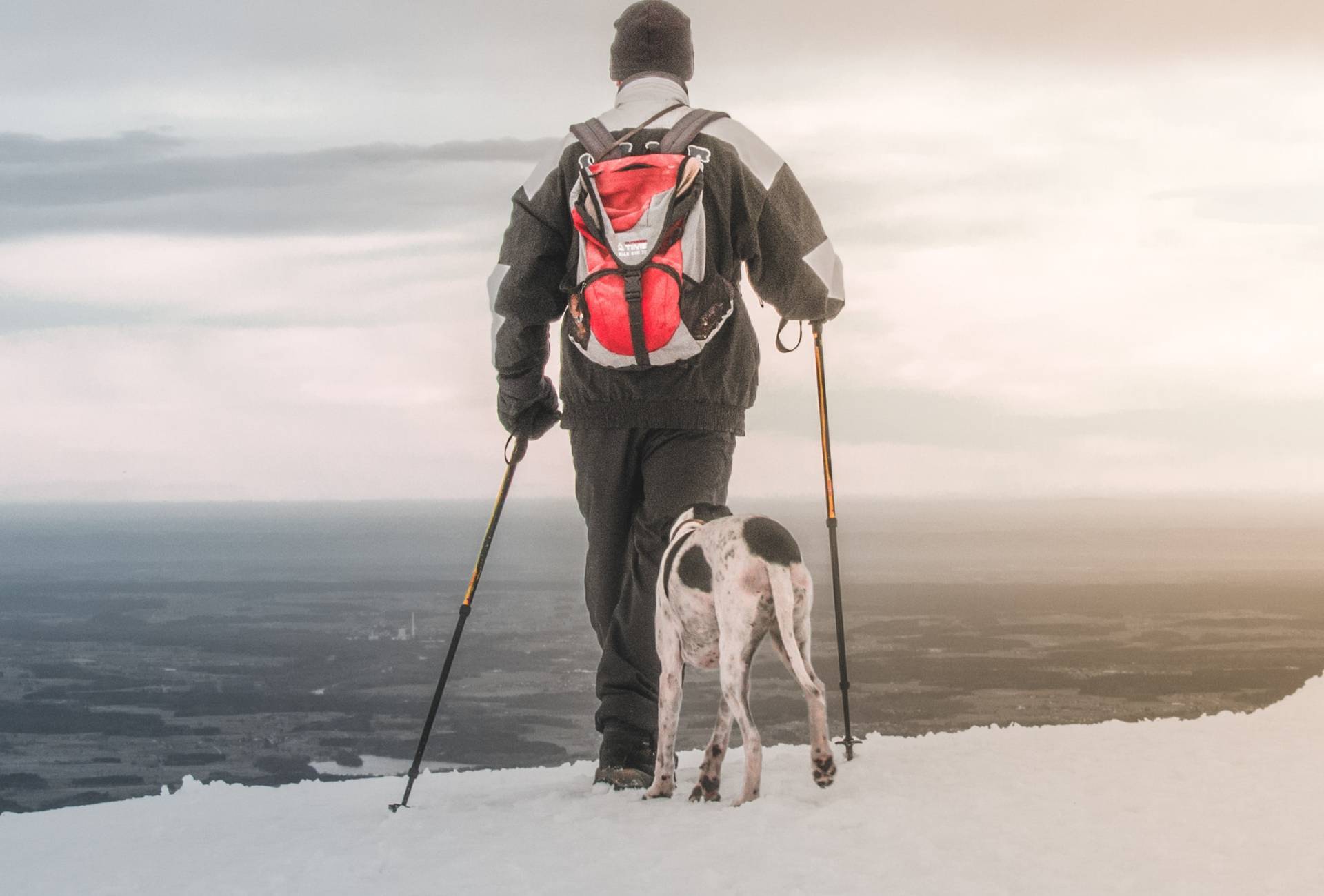 Man is hiking in snowy conditions with a backpack and a dog following.